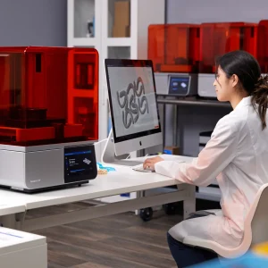 Zahntechnikerin bereitet am Computer einen Druckauftrag neben dem Formlabs Form 4B vor