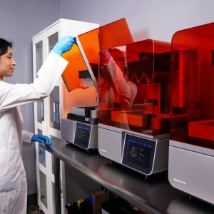 Zahntechnikerin öffnet die Abdeckung eines Formlabs Form 4B in einer Reihe von Dental-3D-Druckern